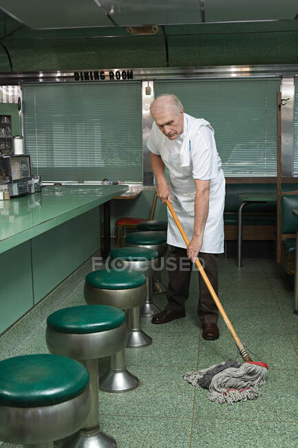 Limpador velho esfregando um chão de restaurante — Fotografia de Stock