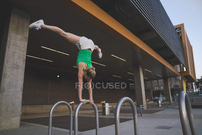 Junge Frau macht Handstand auf Metallstange in urbaner Umgebung — Stockfoto