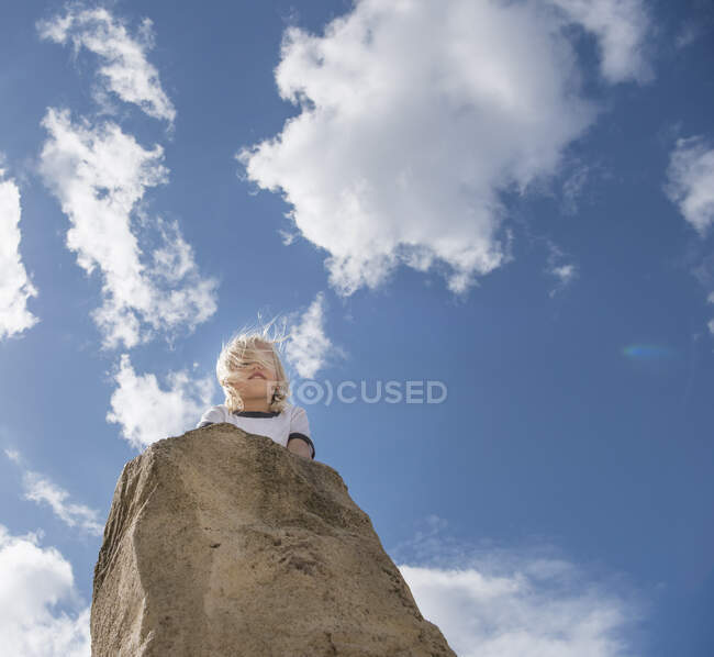 Chico en la cima de la roca mirando hacia otro lado - foto de stock