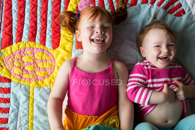 Портрет двух юных сестер, лежащих на одеяле, смеющихся — стоковое фото