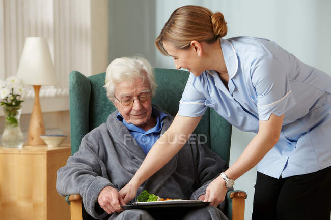 Aide-soignant apportant le repas à un aîné — Photo de stock