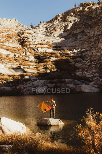 Young male hiker standing on rock in lake with towel, Mineral King, Sequoia National Park, California, USA — Stock Photo