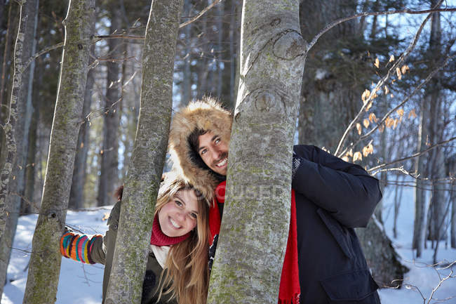 Casal espreitando em torno de troncos de árvore — Fotografia de Stock