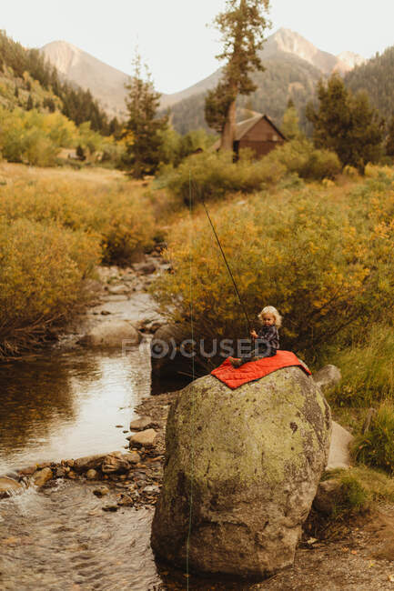 Jeune garçon assis sur la roche près d'un ruisseau, tenant une canne à pêche, Mineral King, Sequoia National Park, Californie, É.-U. — Photo de stock