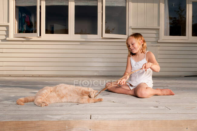 Girl and pet cat playing with stick — Stock Photo