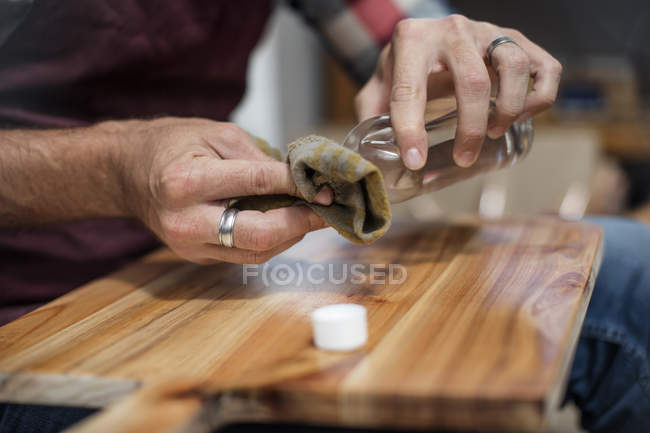 Primer plano del hombre aplicando una mancha de madera a la tabla de cortar en fábrica - foto de stock