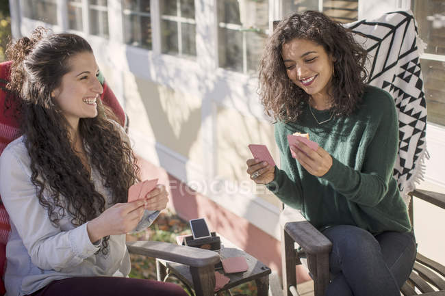 Due giovani amiche che ridono, giocando a carte sul patio — Foto stock
