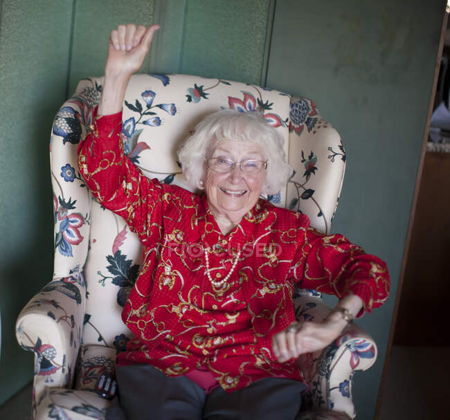 Retrato de mulher idosa sentada na cadeira, sorridente, braço levantado — Fotografia de Stock