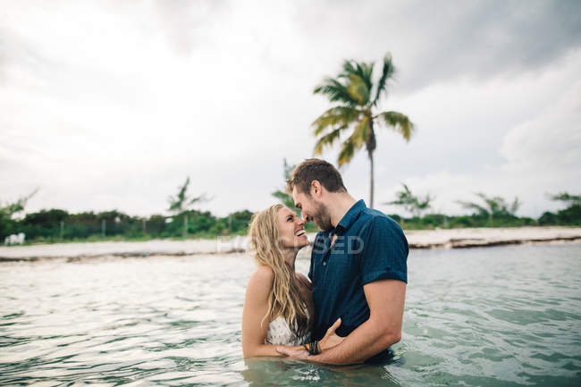 Couple waist deep in water face to face, smiling — Stock Photo