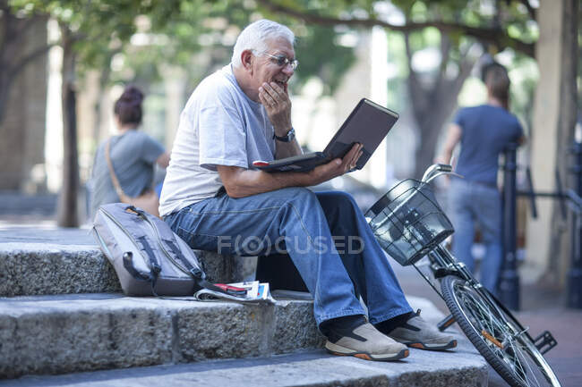 Cape Town, South Africa, elderly man with laptop sitting on steps in city — Stock Photo