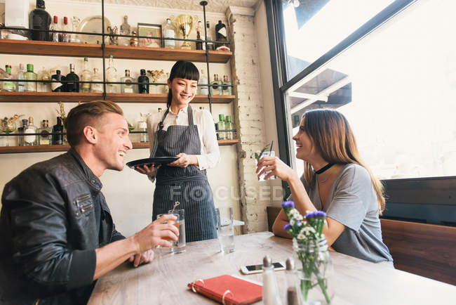Barman feminino servindo jovem casal em bar de coquetéis — Fotografia de Stock