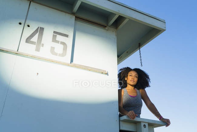 Середня доросла жінка стоїть на вигляд на вежу на пляжі, дивлячись на вигляд — стокове фото