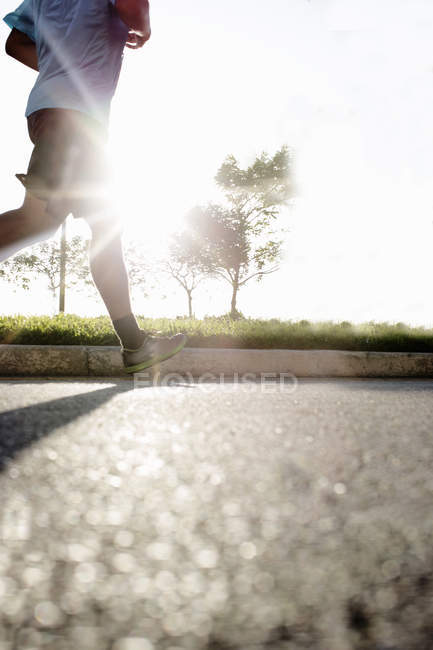 Legs of male runner running on road in backlit — Stock Photo