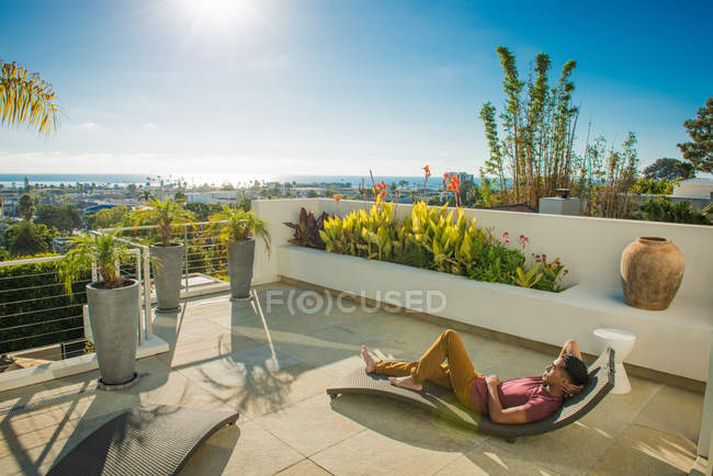 Jovem deitado na espreguiçadeira no jardim do telhado da cobertura, La Jolla, Califórnia, EUA — Fotografia de Stock