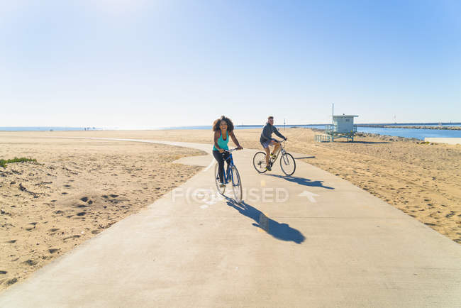 Casal de ciclismo ao longo do caminho na praia — Fotografia de Stock