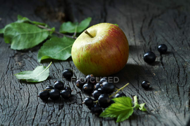 Apples and blackcurrants on old wooden surface — Stock Photo