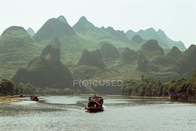 Лодка парусный спорт вдоль реки Лицзян с зелеными холмами на горизонте, Китай — стоковое фото