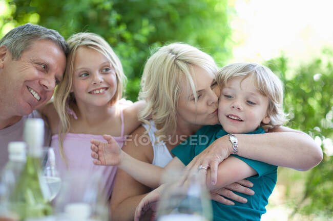 Mother kissing son at table outdoors — Stock Photo