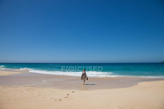 Mujer sola en una playa, caminando hacia el mar - foto de stock