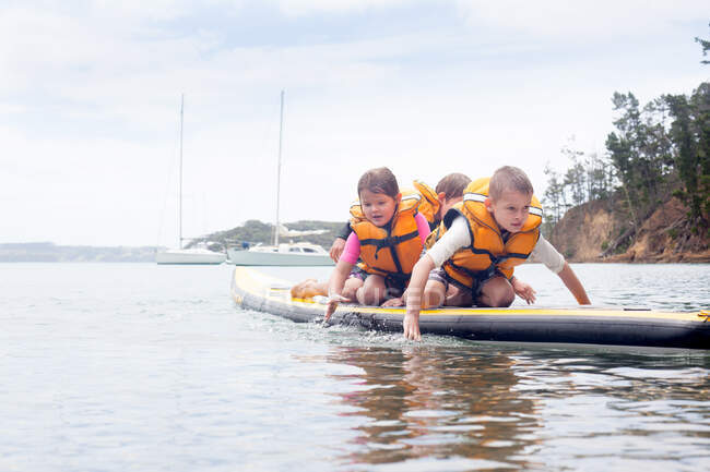Fratelli e sorelle paddleboarding in ginocchio in mare — Foto stock