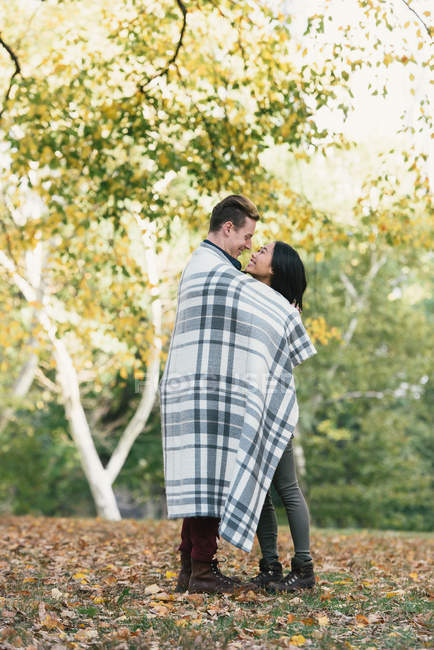 Romântico casal adulto médio envolto em cobertor no parque — Fotografia de Stock