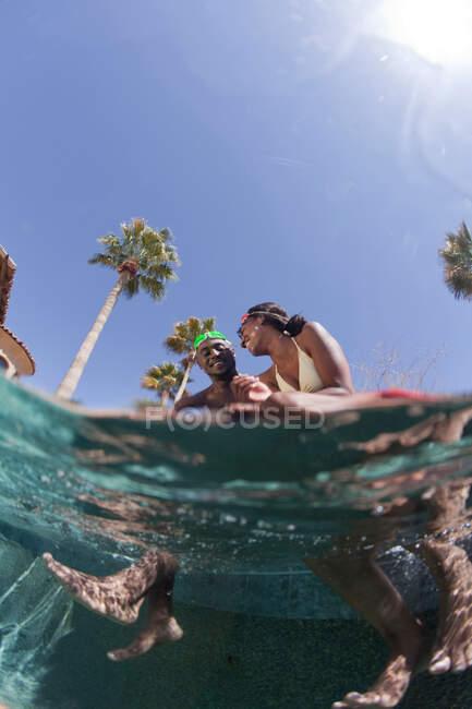 Coppia giovane seduta sul bordo della piscina, vista sul livello della superficie — Foto stock