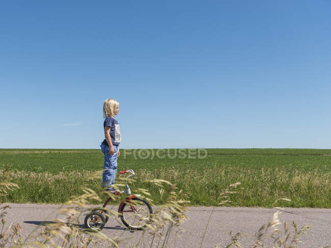 Vista lateral do menino em pé no triciclo na área rural — Fotografia de Stock