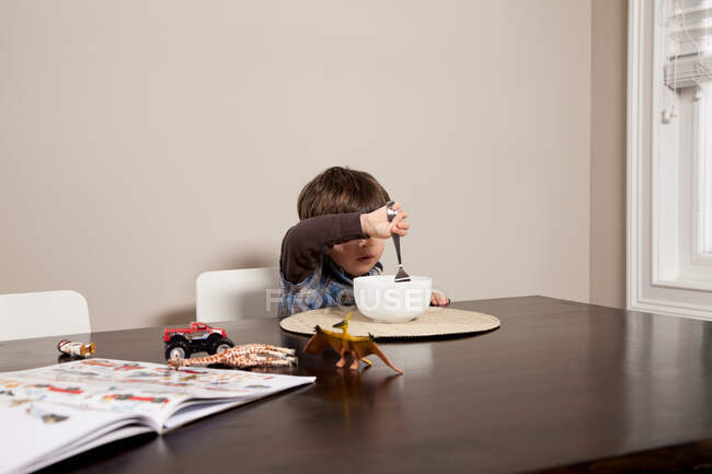 Garçon à table avec bol de nourriture et jouets — Photo de stock
