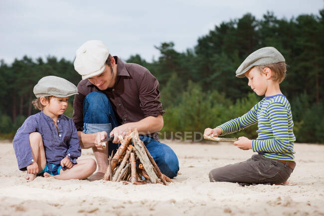 Батько і сини роблять багаття на пляжі — стокове фото