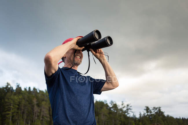 Senior man looking through binoculars toward coast of Maine, USA — Stock Photo