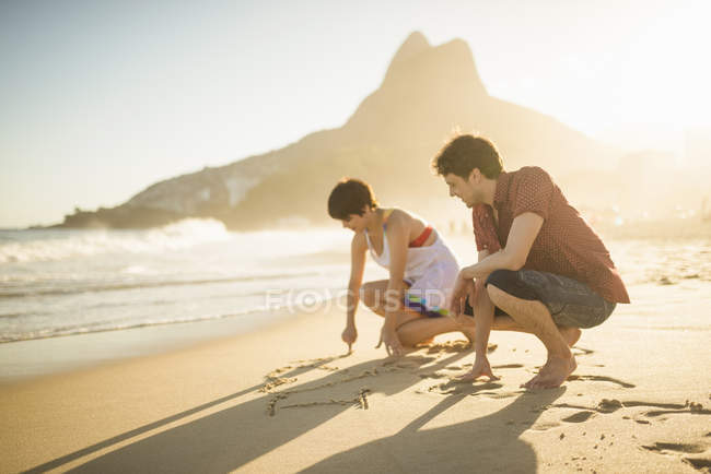 Junges paar schreibt auf sand, ipanema beach, rio, brasilien — Stockfoto