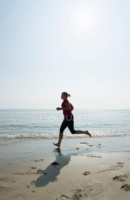 Mulher correndo na praia no dia ensolarado — Fotografia de Stock