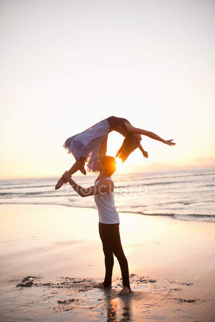 Giovane uomo che solleva partner di danza sulla spiaggia illuminata dal sole — Foto stock