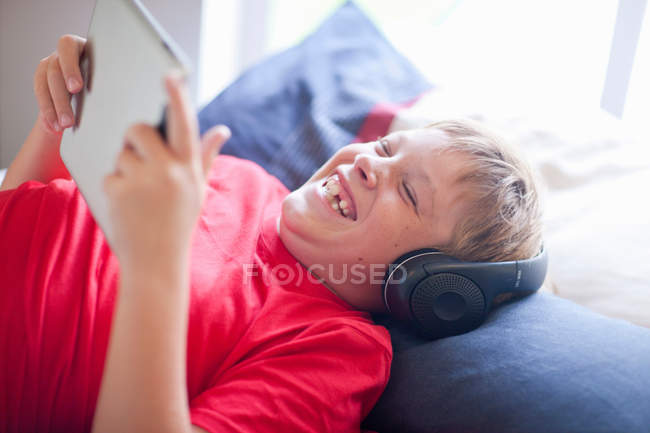Мальчик на кровати слушает музыку и пользуется цифровым планшетом — стоковое фото