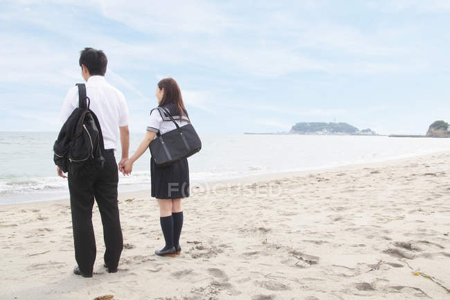 Jeune couple tenant la main sur la plage, vue arrière — Photo de stock