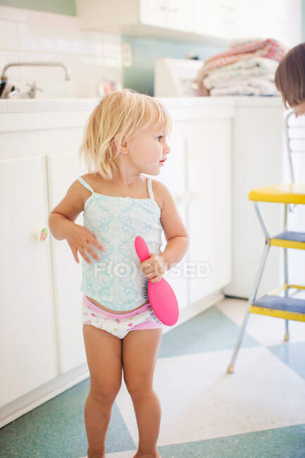 Menina vestindo colete e calcinhas segurando escova de cabelo — Fotografia de Stock