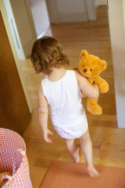 Girl carrying teddy bear in bedroom — Stock Photo