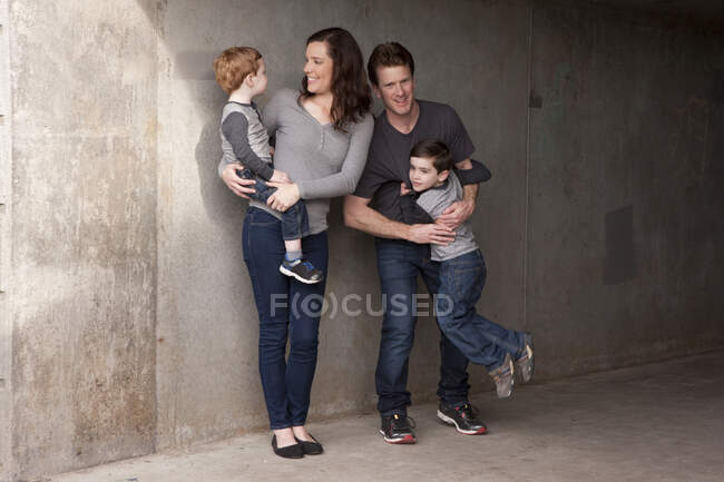 Familia de pie junto a la pared, sonriendo - foto de stock