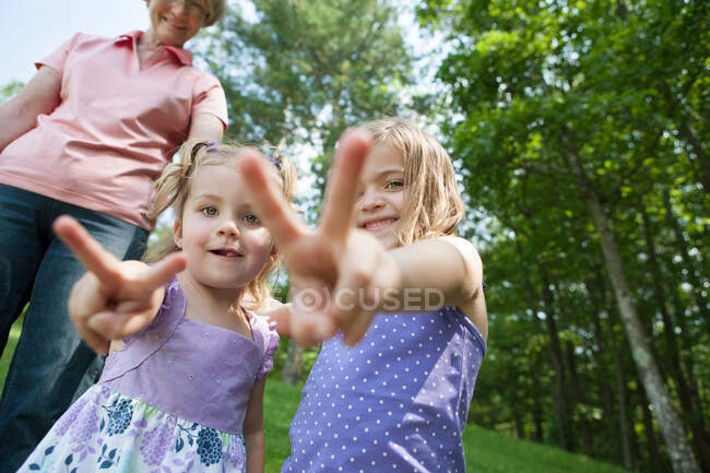 Девушки делают знак победы с бабушкой на заднем плане — стоковое фото