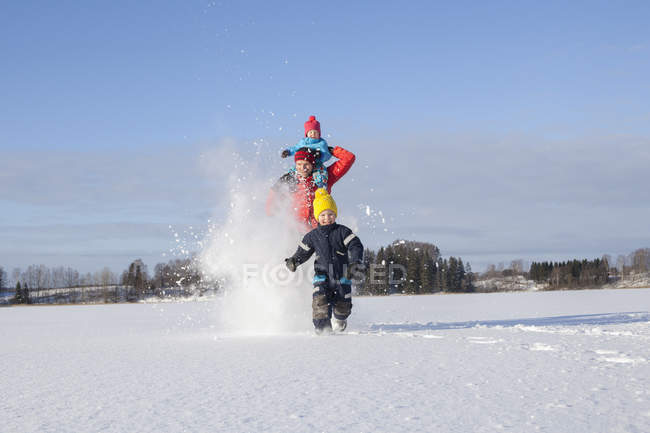 Padre y dos hijos tonteando, corriendo por el paisaje cubierto de nieve - foto de stock