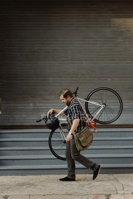 Male cycle messenger carrying cycle on sidewalk — Stock Photo