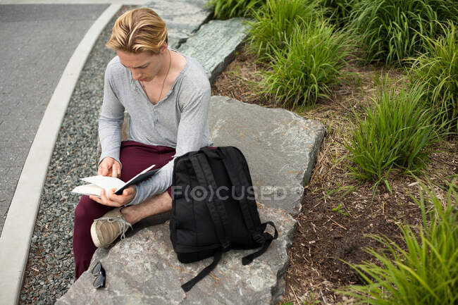 Молодий чоловік вивчає текстову книгу в парку — стокове фото