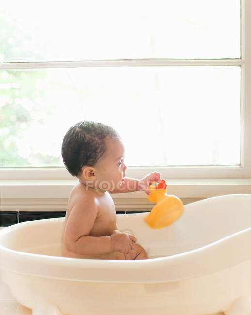 Bambina seduta in bagno in possesso di anatra di gomma — Foto stock