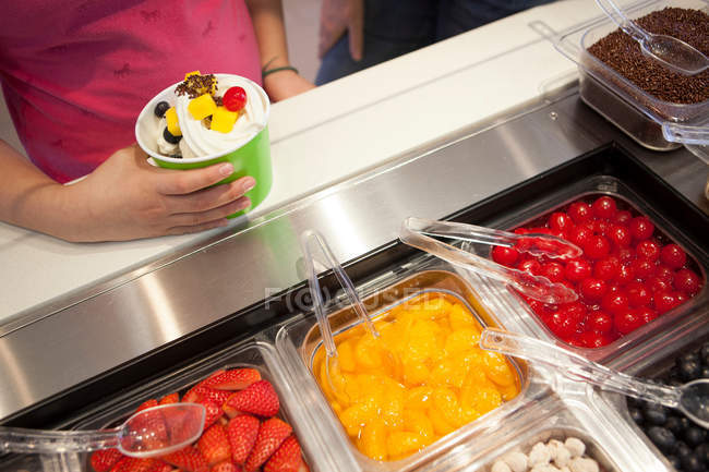 Kid standing with frozen yogurt and toppings — Stock Photo