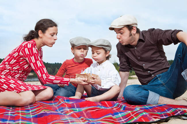 Мальчик и семья с праздничным тортом на одеяле для пикника — стоковое фото