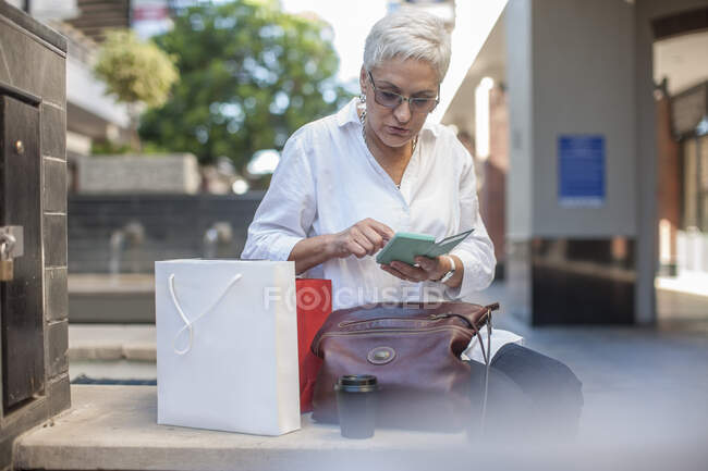 Cidade do Cabo África do Sul, mulher idosa sentada com sacos de compras, em seu celular — Fotografia de Stock