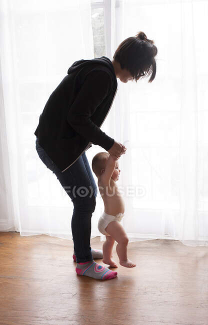Young female babysitter helping baby boy toddle at home — Stock Photo