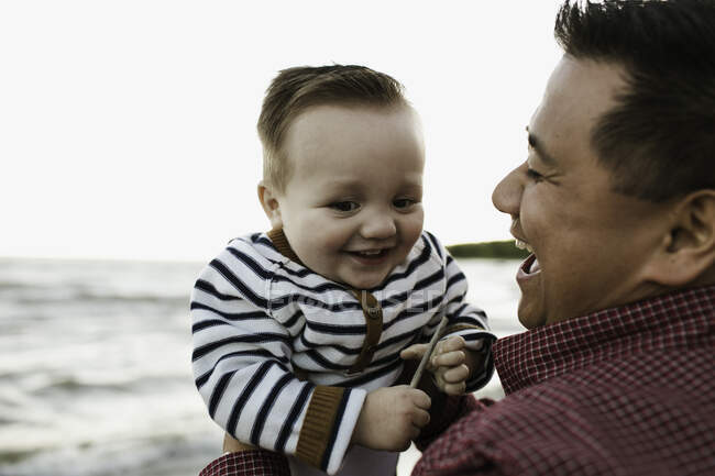 Отец на пляже держит улыбающегося мальчика — стоковое фото