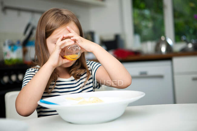 Girl drinking orange juice at table — Stock Photo