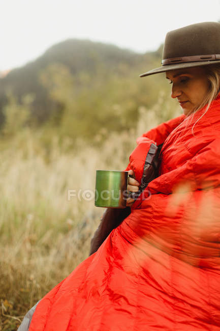 Жінка сидить у сільській обстановці, загорнуті в спальний мішок, тримаючи олов'яні гуртки, мінеральне цар, Національний парк Секвойя, Каліфорнія, США — стокове фото